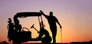 sunset siloette of a man leaning on a golf cart holding a golf club