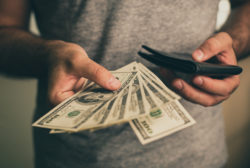 A man holds dollars and black wallet in his hands